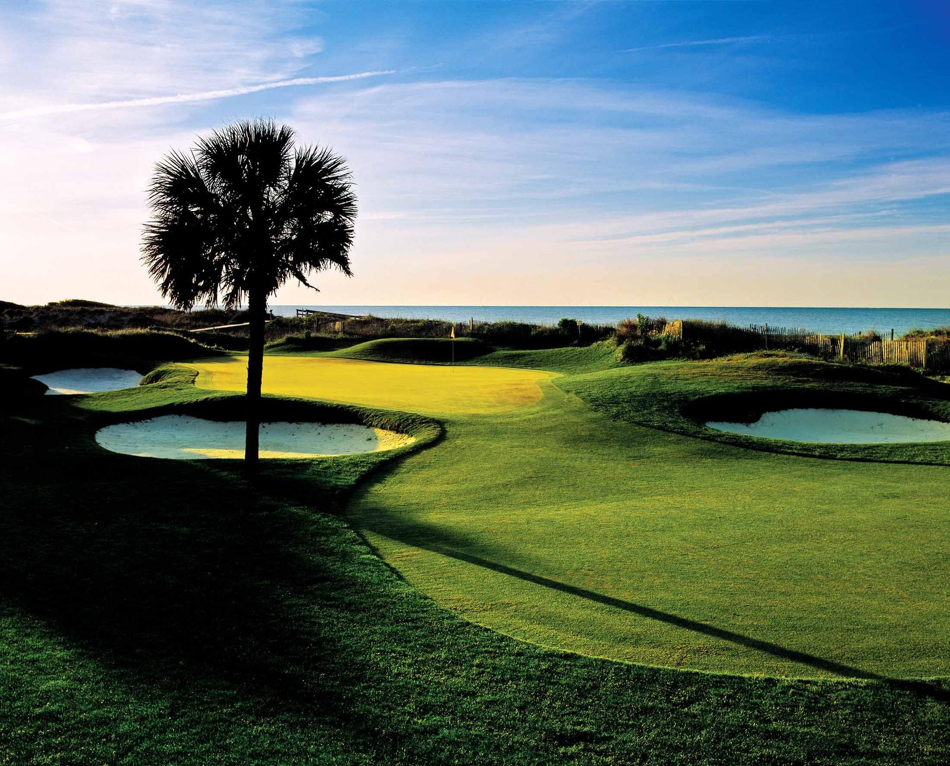 Sen setting over a manicured green surrounded by bunkers with sea views
