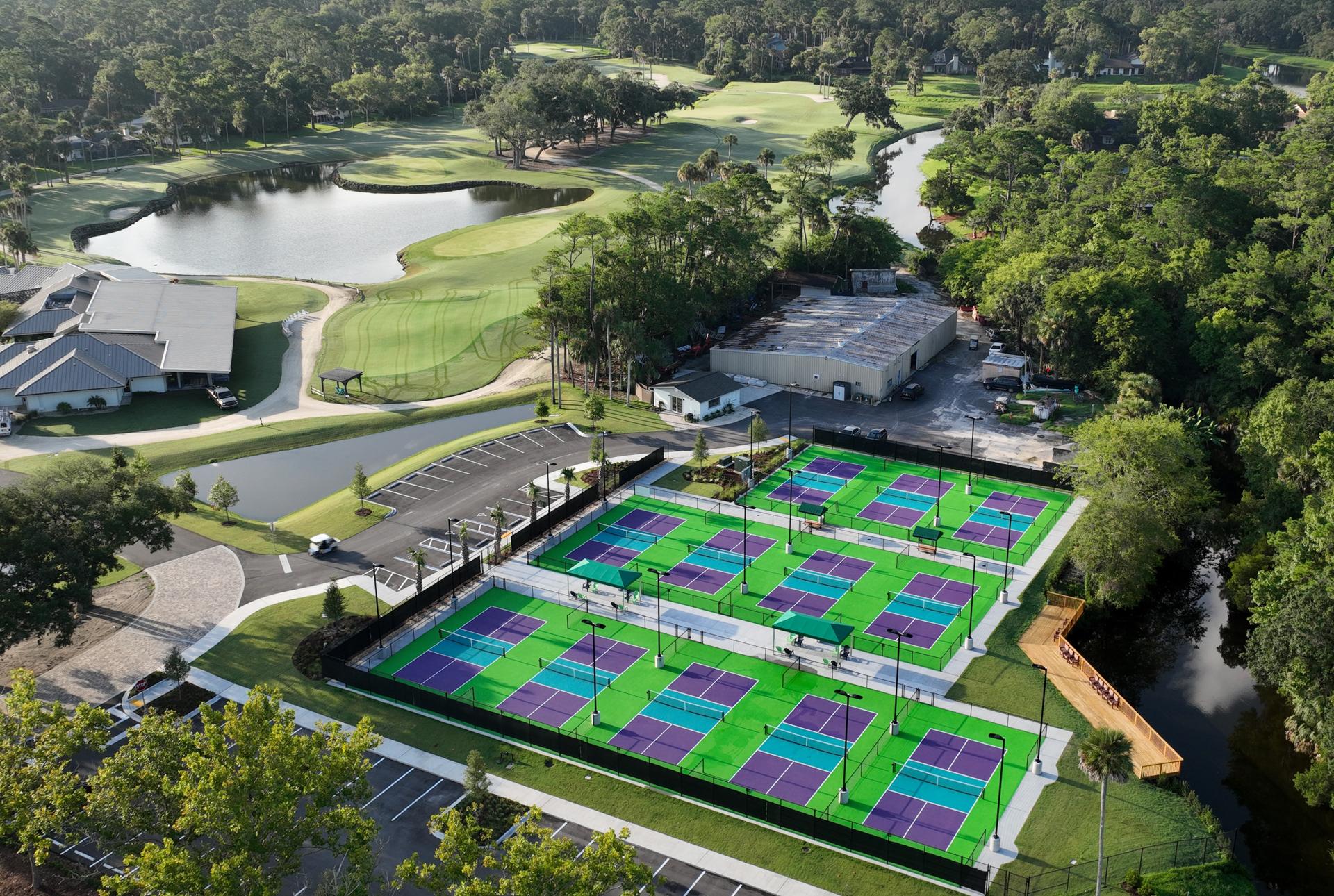 Birdseye view of multiple tennis courts at the resort with their on sight golf course in the distance