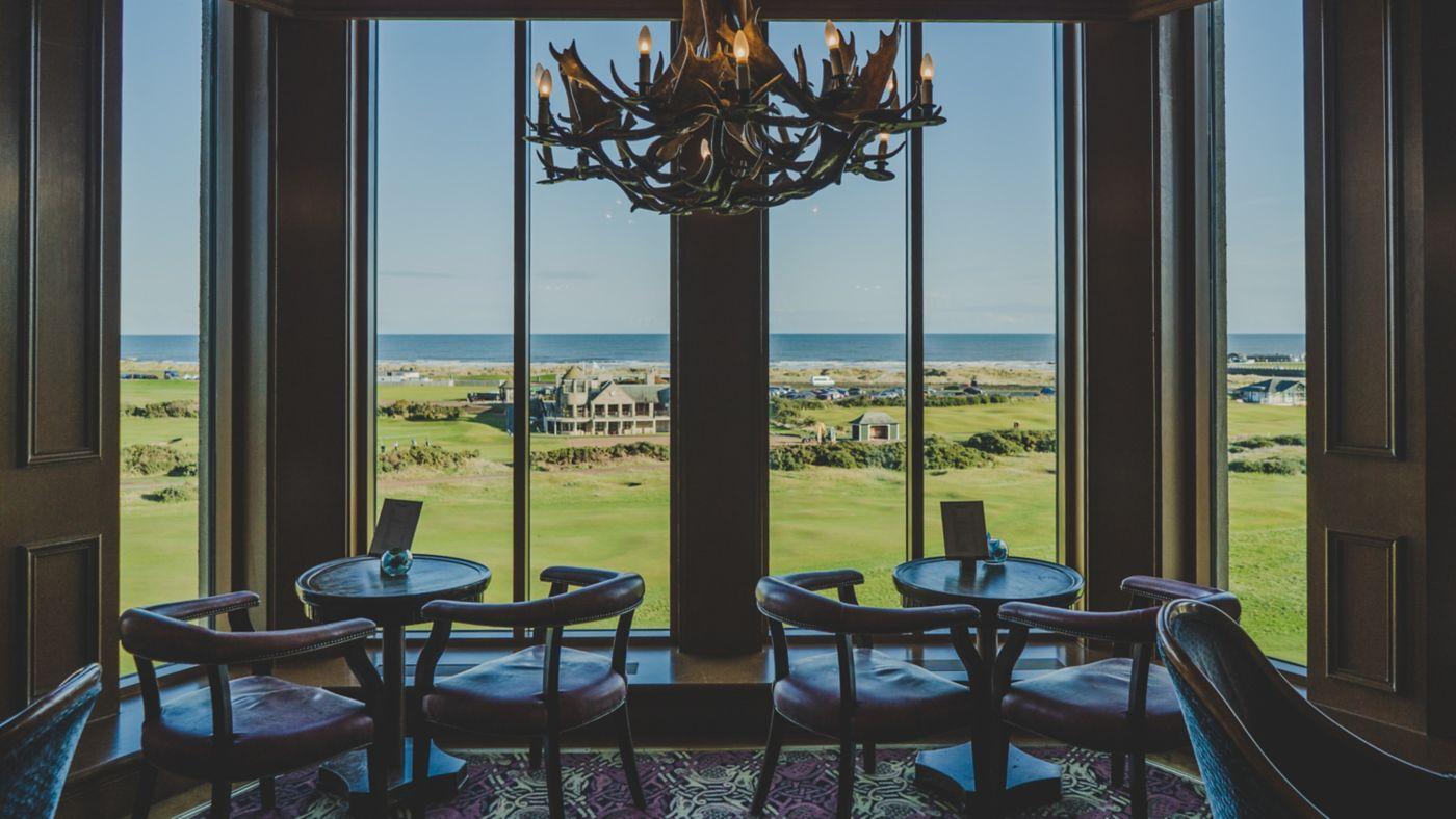 A cozy seating area offers stunning views of the golf course and ocean through large panoramic windows.