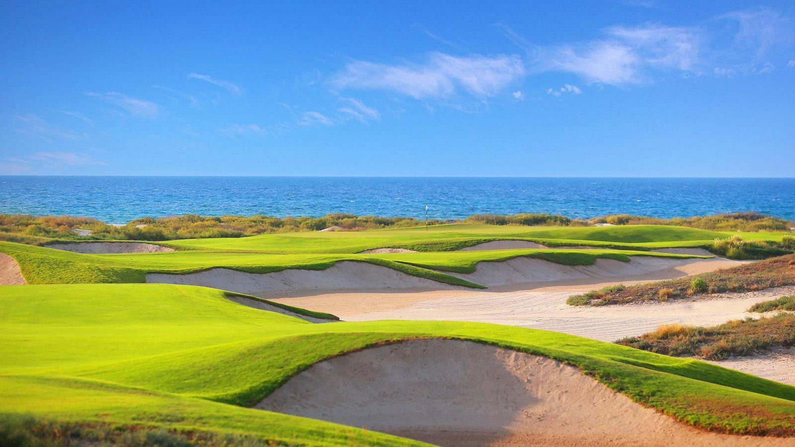 Green golf course near coastline and blue sky