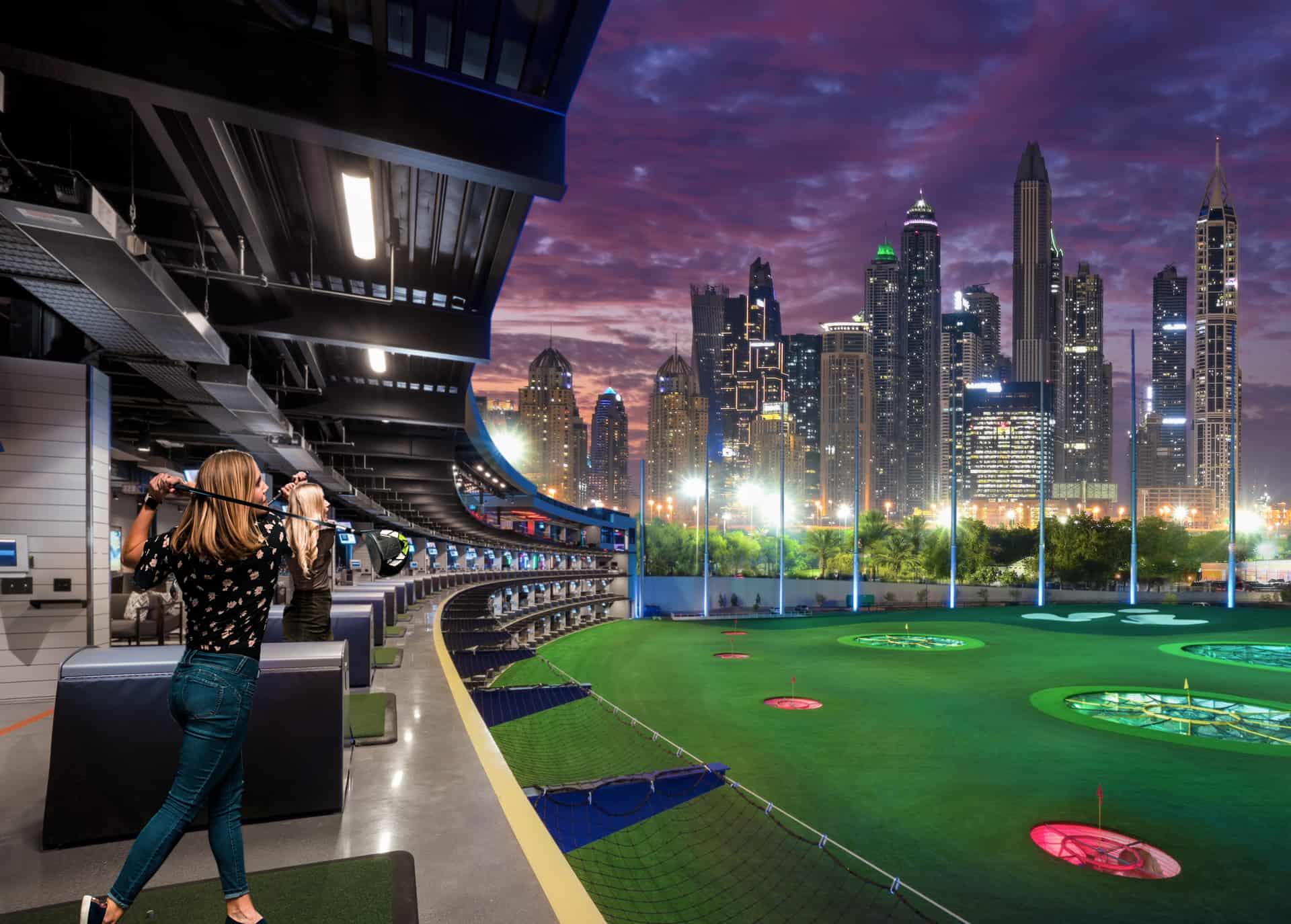 Topgolf-style driving range with illuminated city view