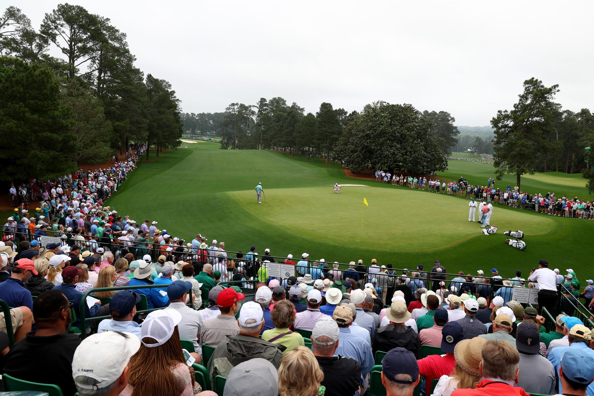 Three players on an undulating green surrounded by crowds at The Masters