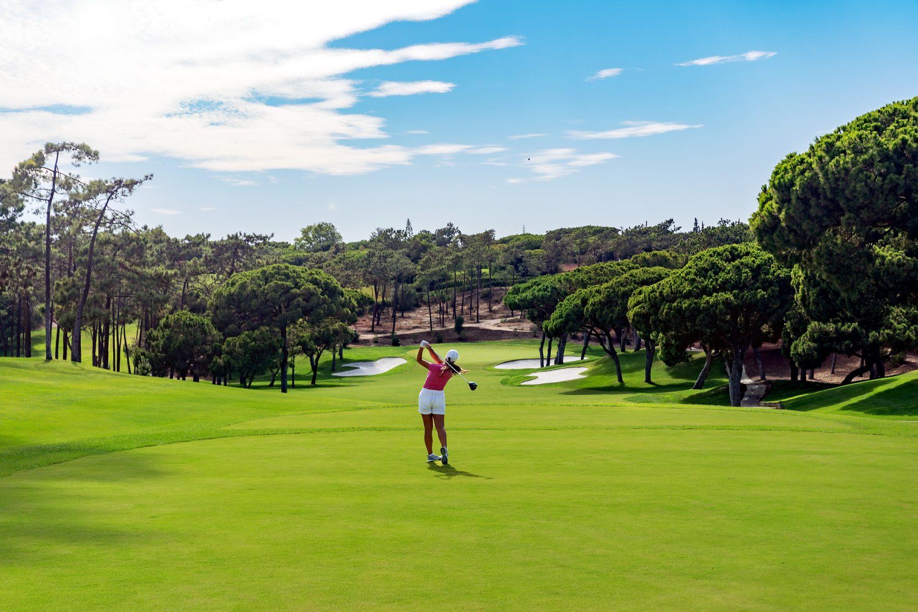 Golfer swings towards a smooth green on a manicured fairway littered with sand bunkers