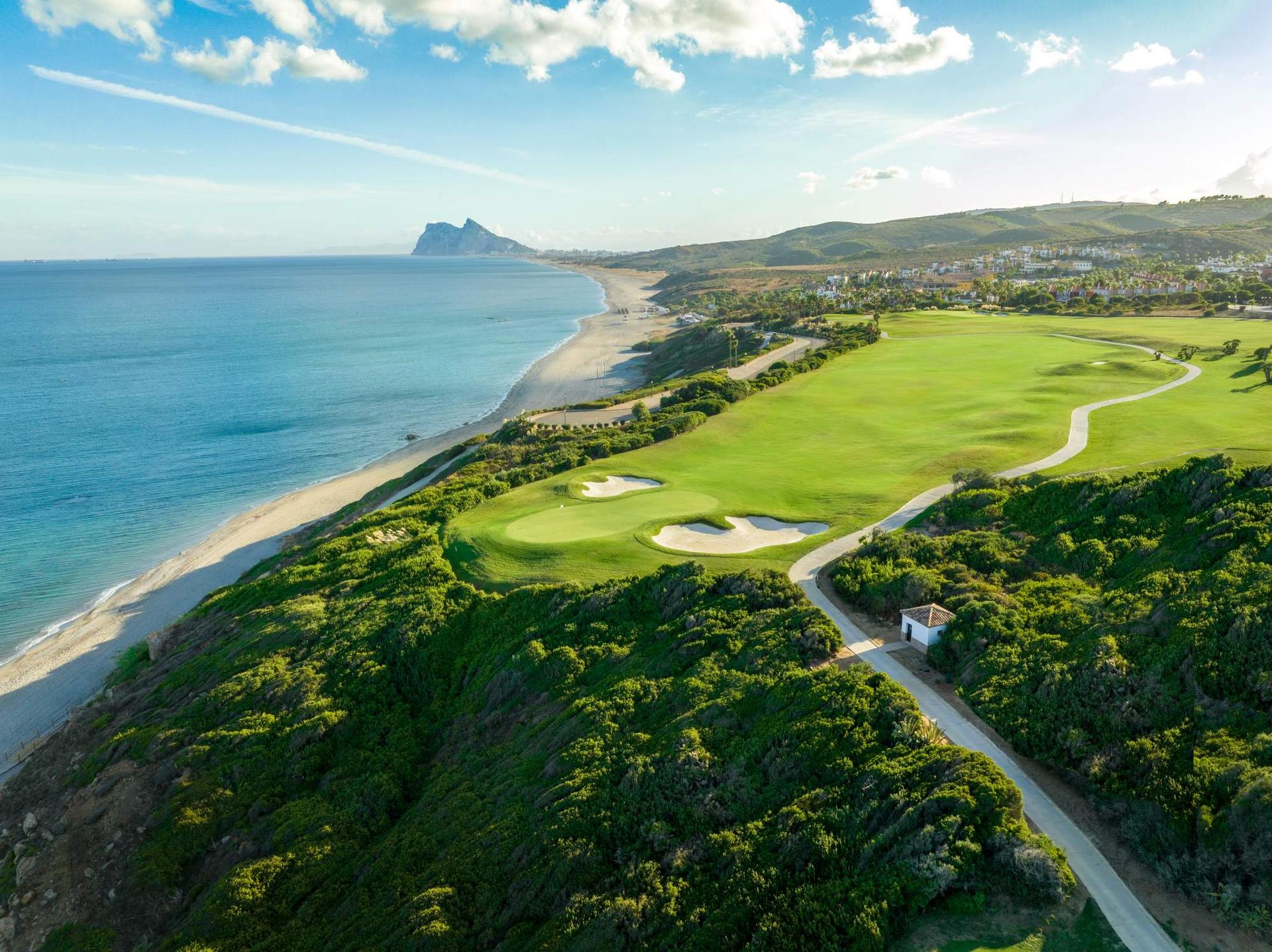 A wide fairway leading to a smooth green being sandwiched by bunkers with coastal views