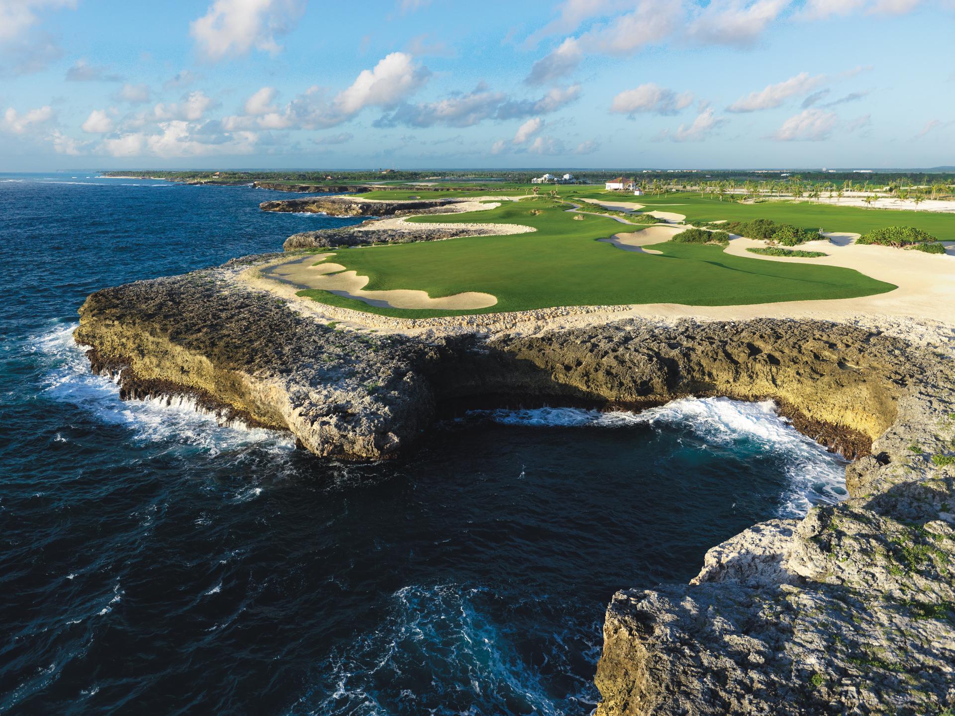 A smooth green surrounded by sand bunkers with coastal views