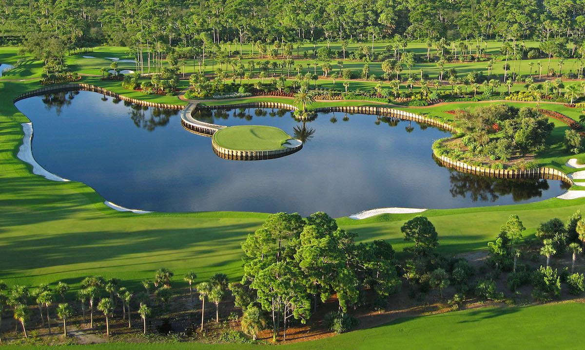 An aerial view shows a striking island green surrounded by a vast reflective lake and dense trees.