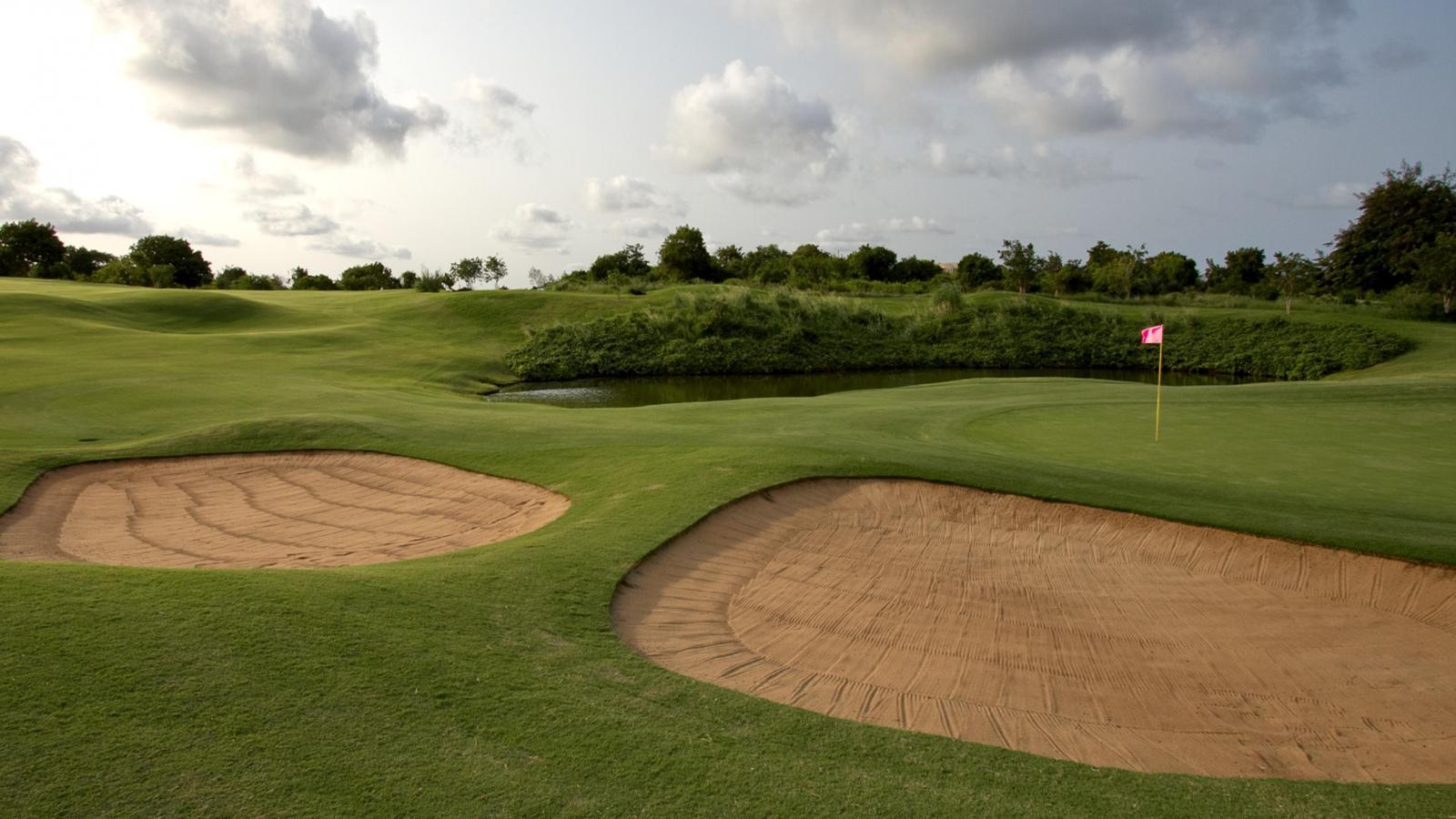 A serene golf green with sand bunkers under a cloudy sky.