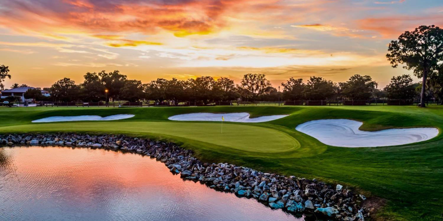 Sun setting over a green sandwiched between bunkers and a water hazard