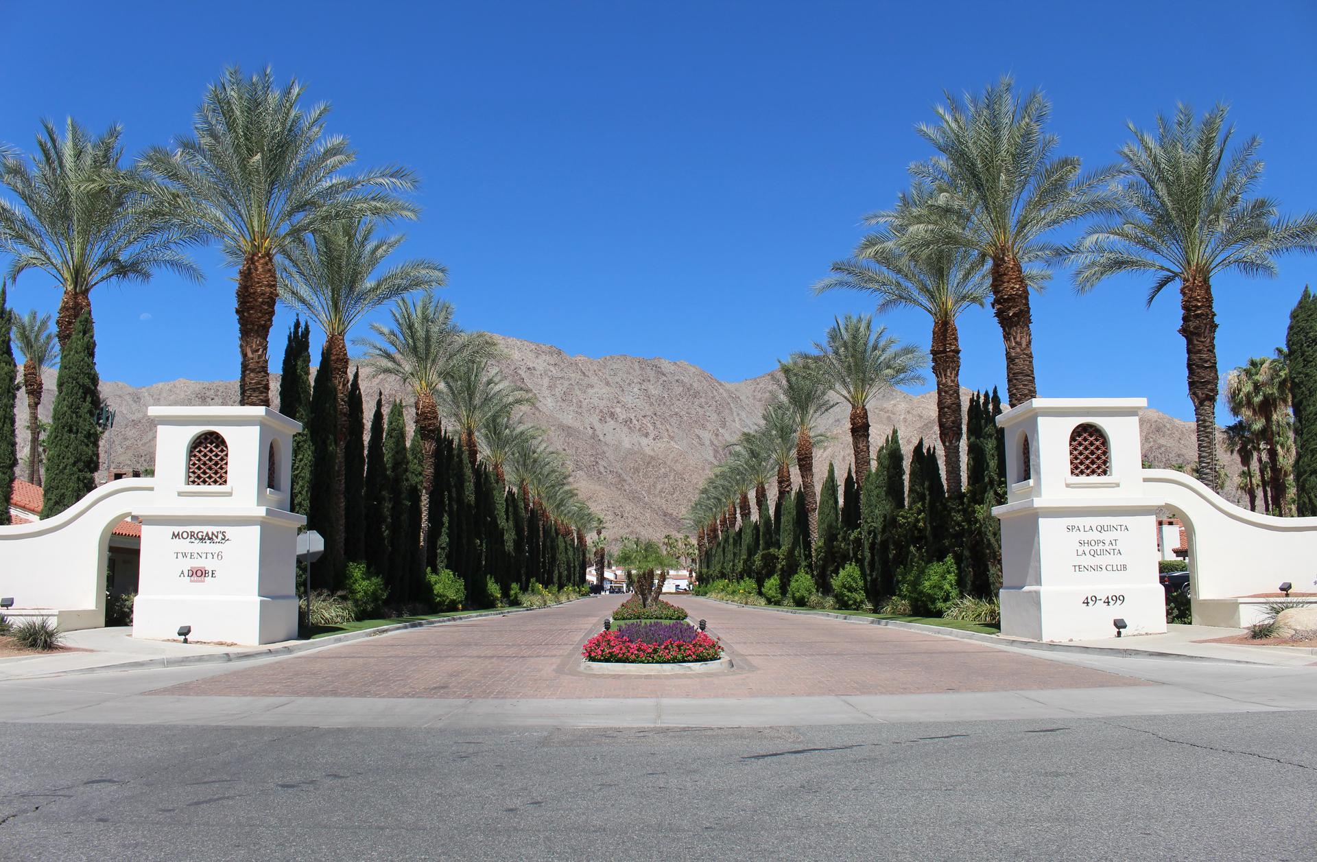 Grand entrance to the La Quinta Resort with the driveway being sandwiched by palm trees.