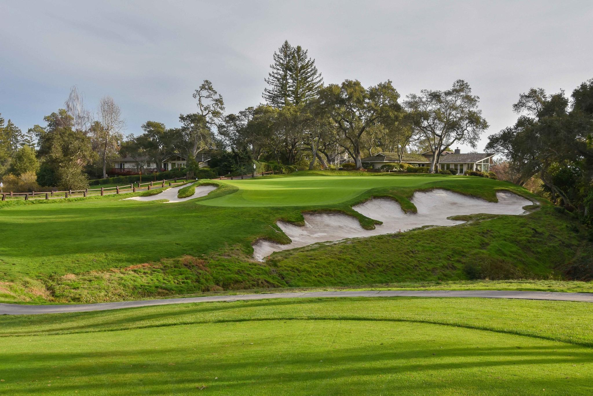 A large uniquely shaped slanted sand bunker placed next to a well maintained green