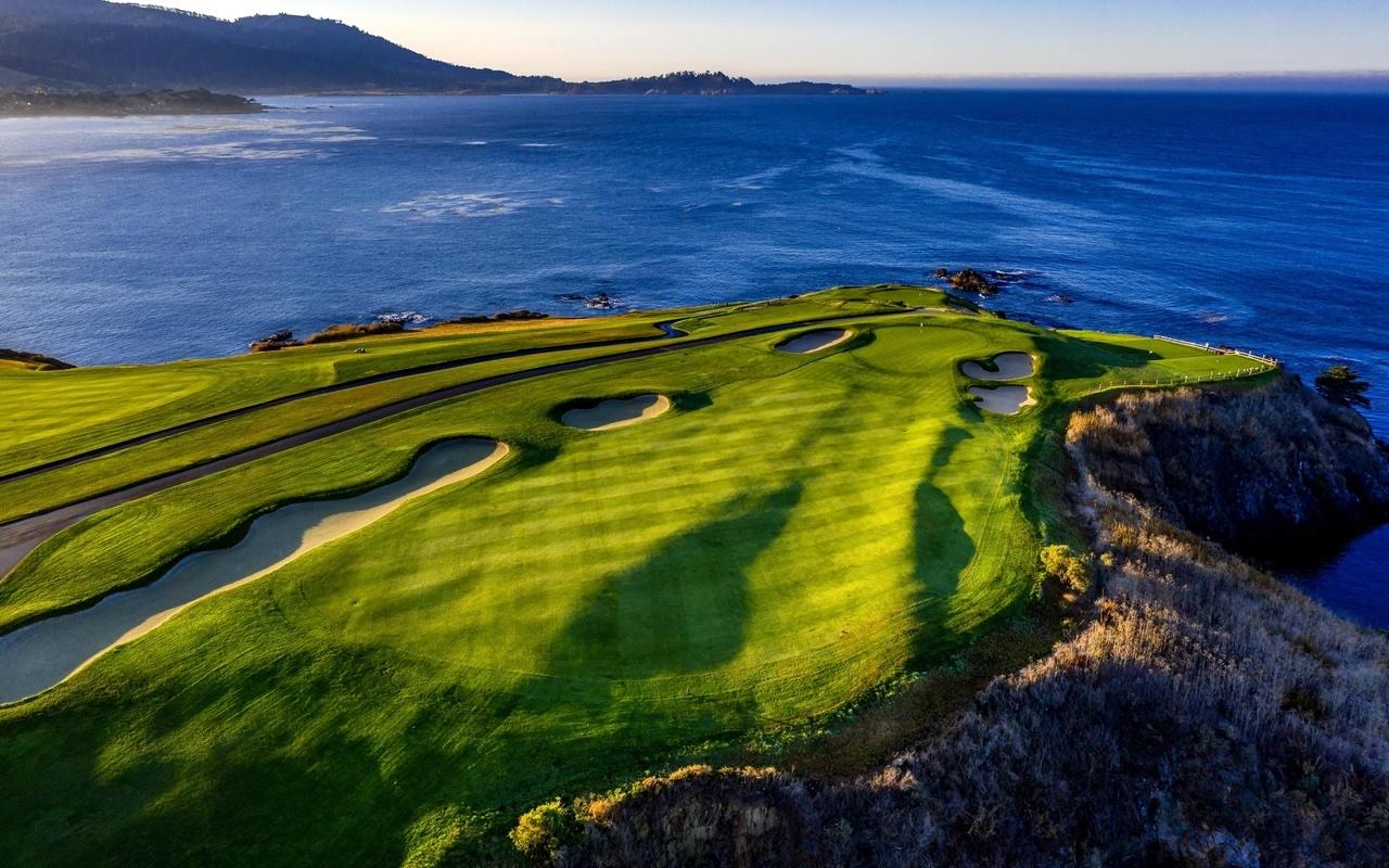 Overhead shot of a wide fairway nestled with sand bunkers leading to a smooth green with sea views