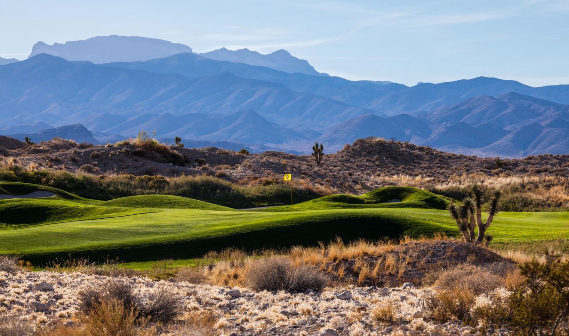 Extreme mountains towering over a smooth green surrounded by rolling dunes