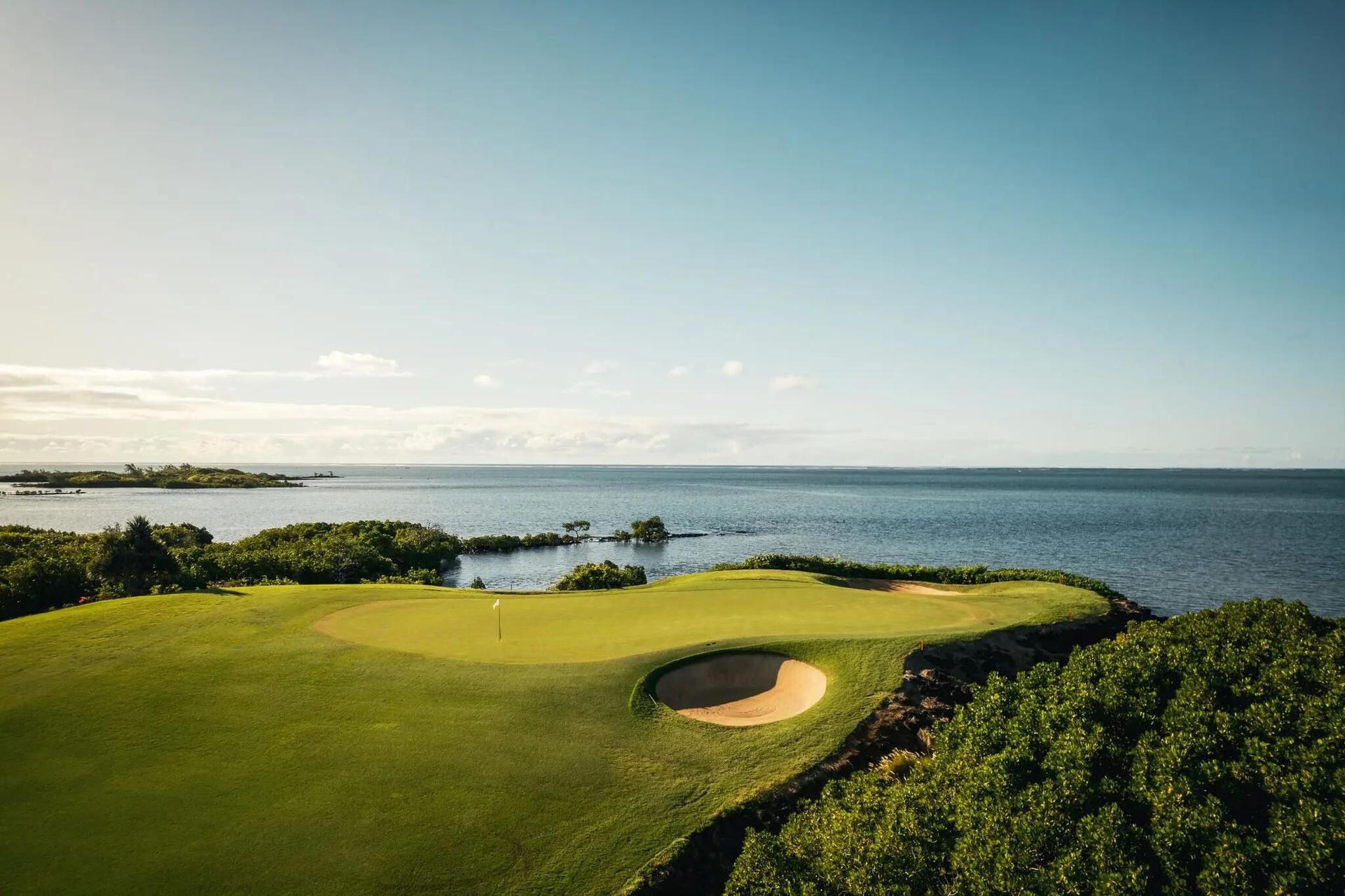 A smooth green surrounded by sand bunkers with coastal views