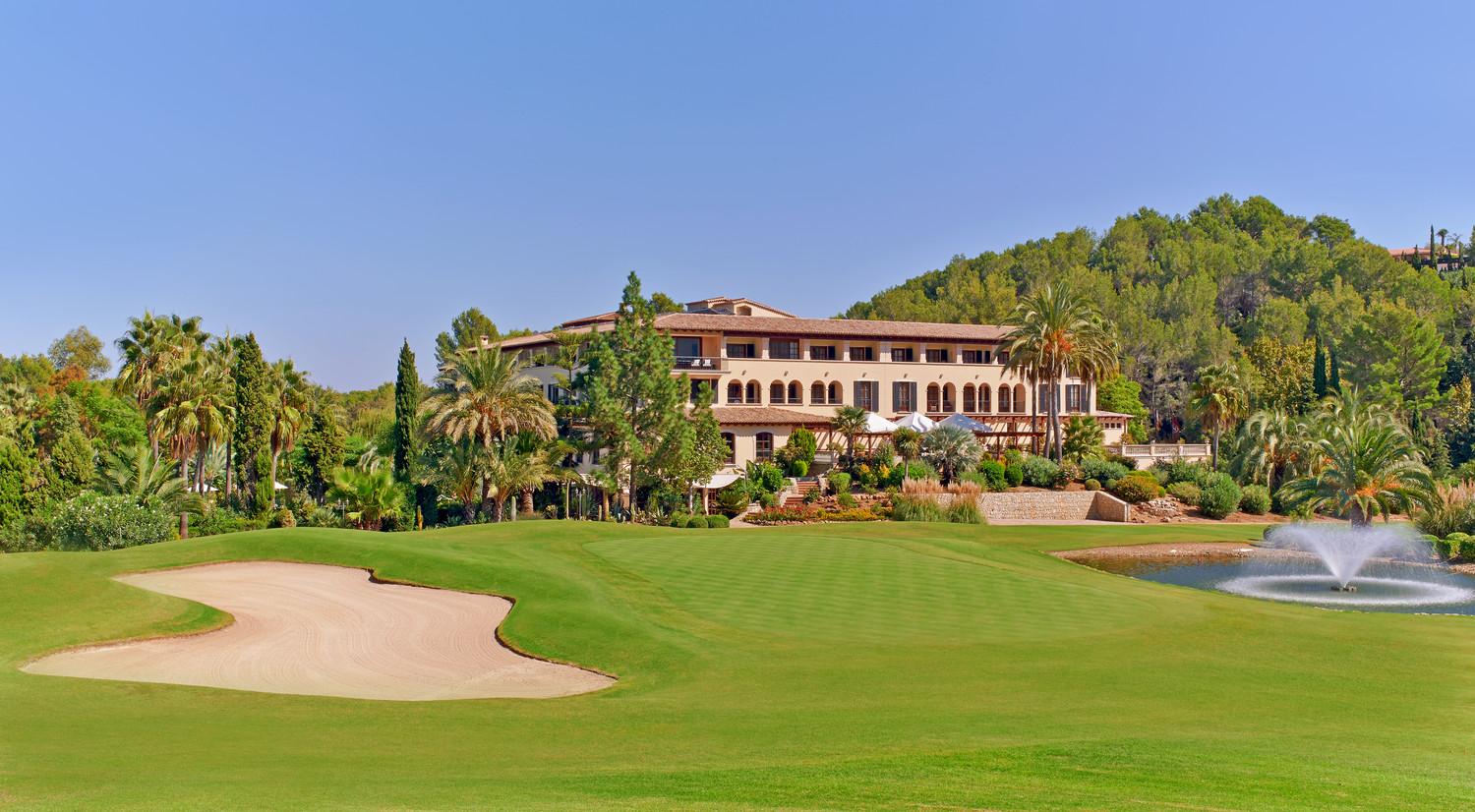 Manicured fairway and green with bunker, water hazard and clubhouse all surrounded by lush greenery