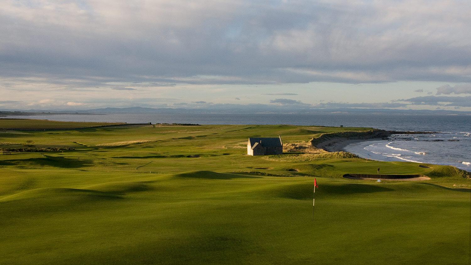 Rolling fairways lead to the shoreline with a lone stone building adding character to the coastal landscape.