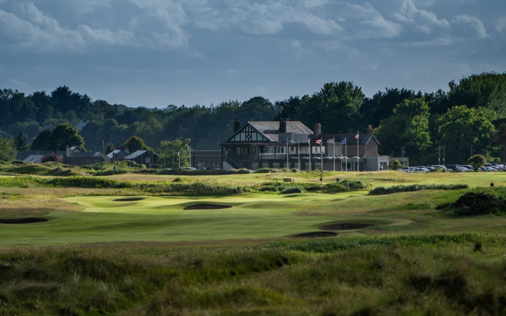 A classic golf clubhouse surrounded by lush trees and links fairways.