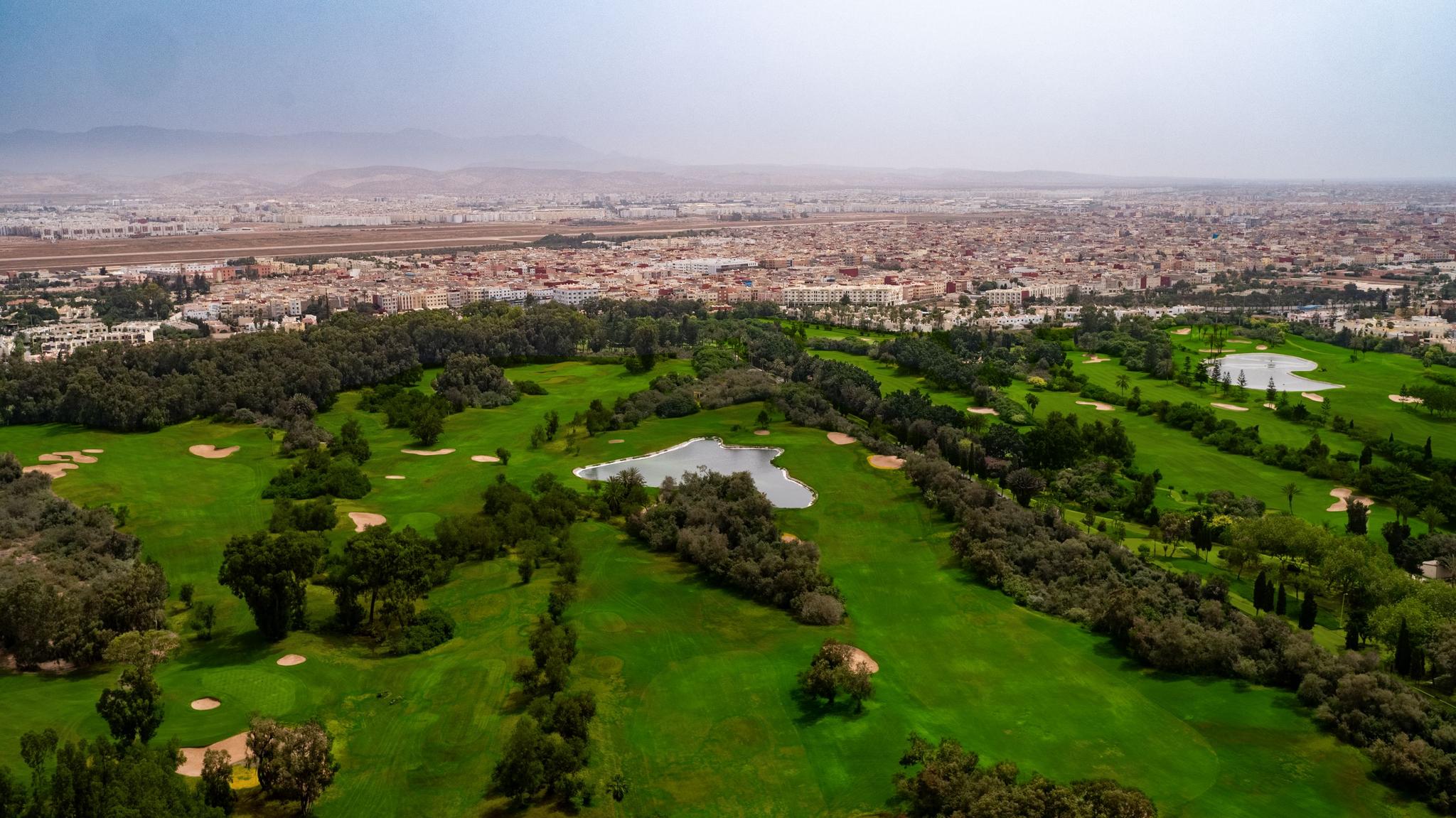 A sprawling golf course lies next to a bustling cityscape.