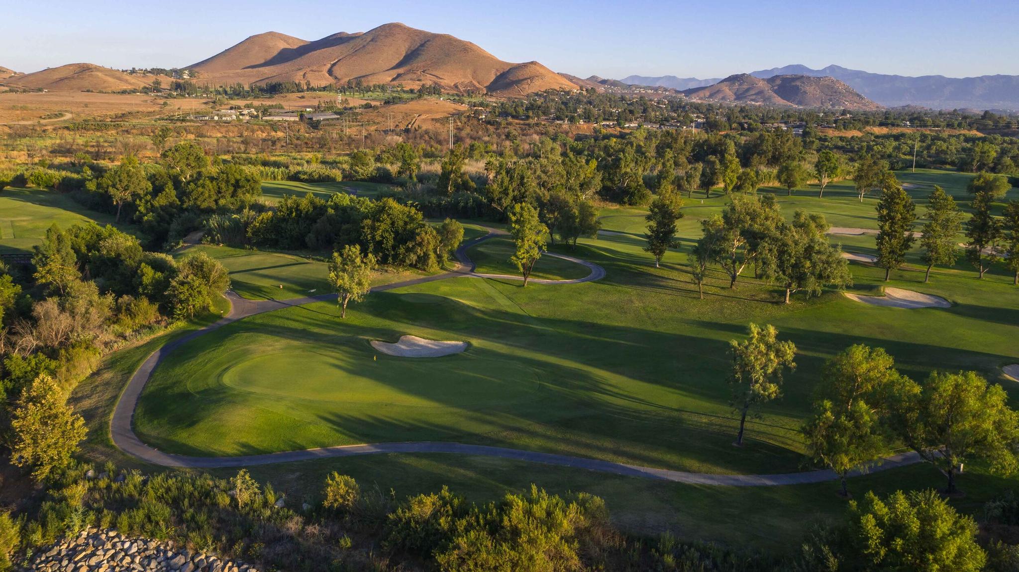 A wide golf course nestled among rolling hills and scattered trees.