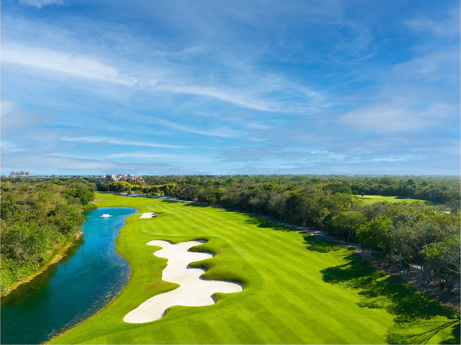 A long, open fairway bordered by dense jungle with a bright blue water hazard running alongside it.