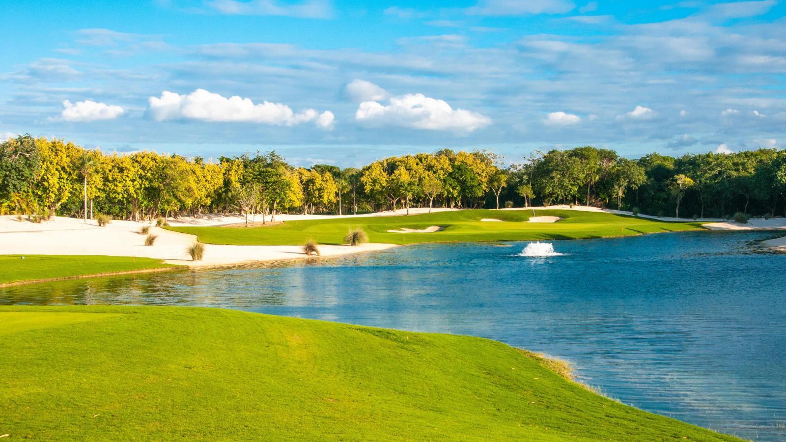A serene golf hole with pristine white sand bunkers and a reflective lake surrounded by vibrant greenery.