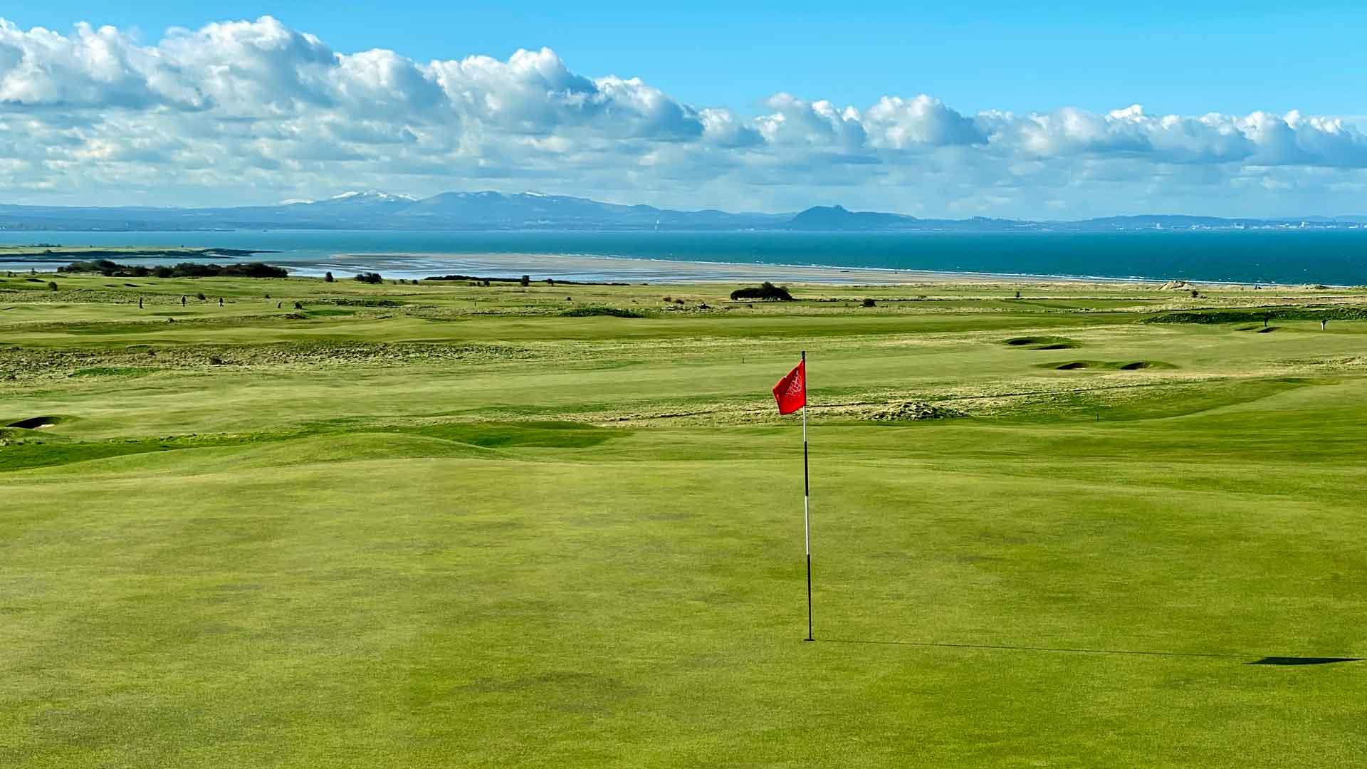 Manicured green with coastal views in the distance underneath blue skies