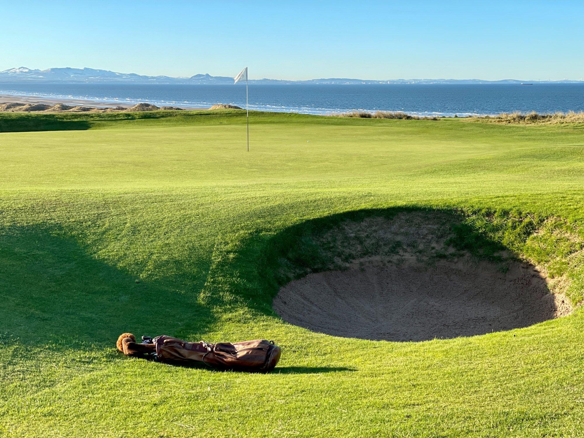 A challenging greenside bunker awaits golfers with the sea glistening in the background.