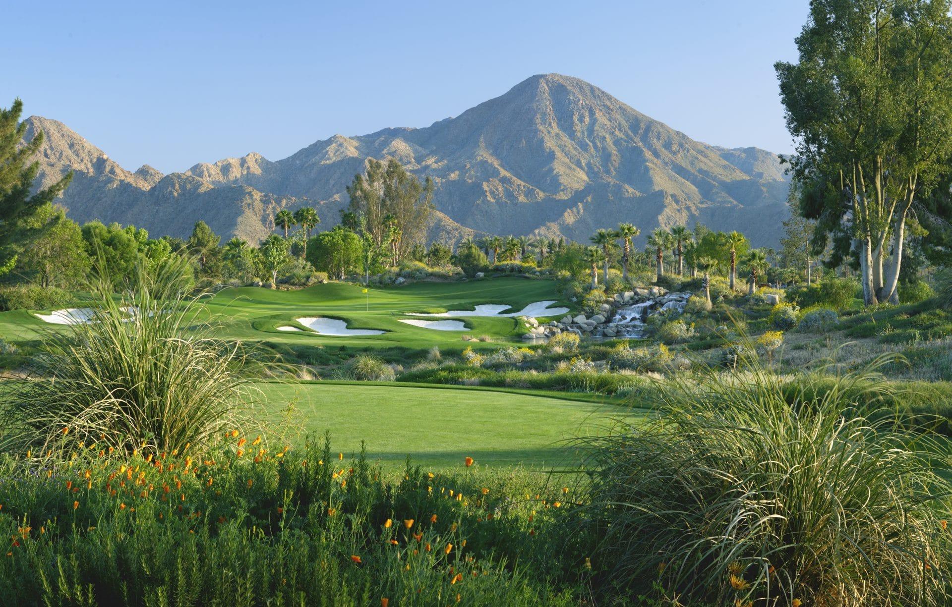 A pristine course with lush greenery, white sand bunkers, and a backdrop of rocky desert peaks.