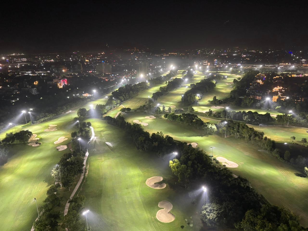 A night-lit golf course glowing brightly against the city skyline.