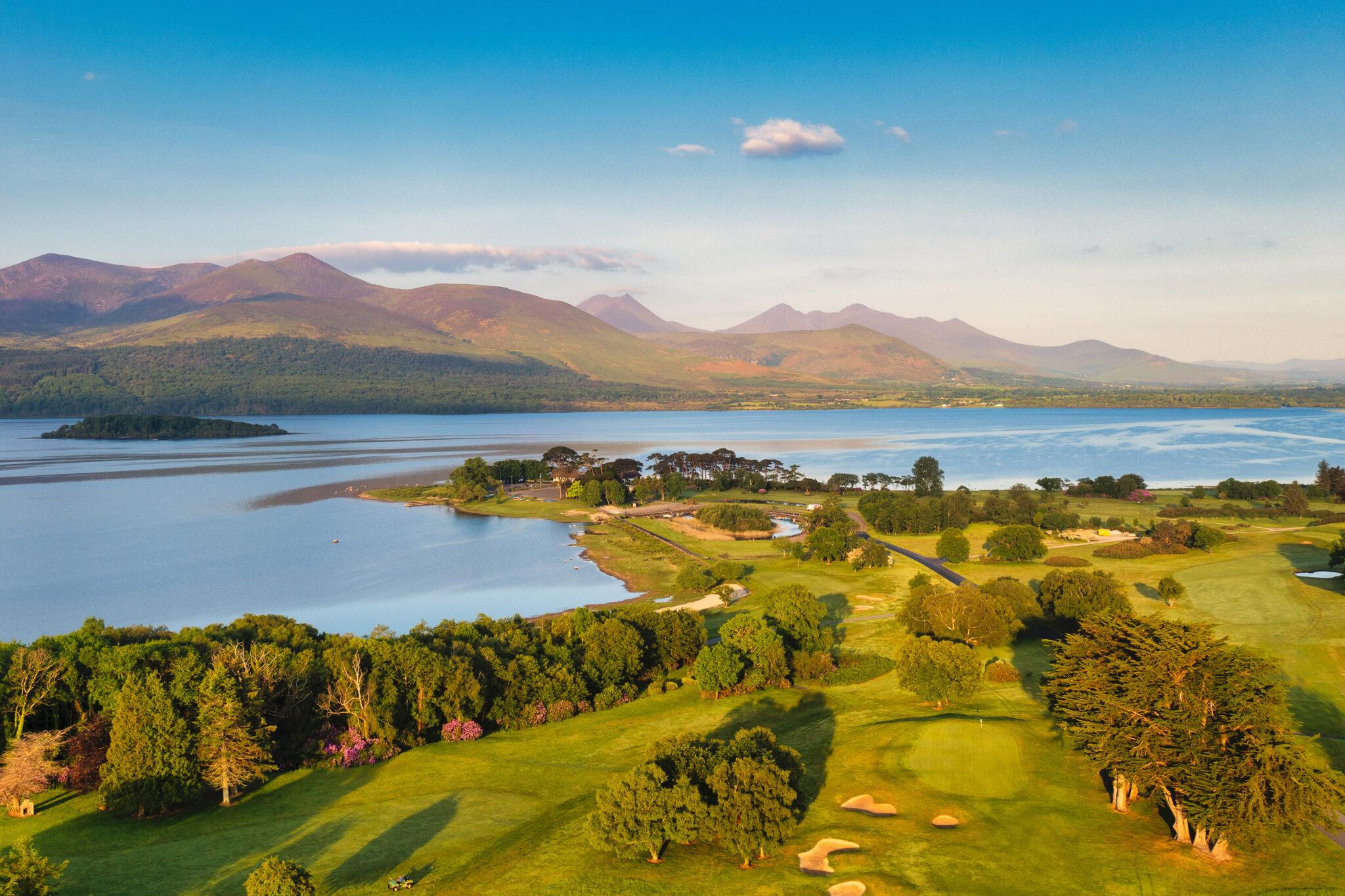 Golden light over lush fairways with mountains in the distance.