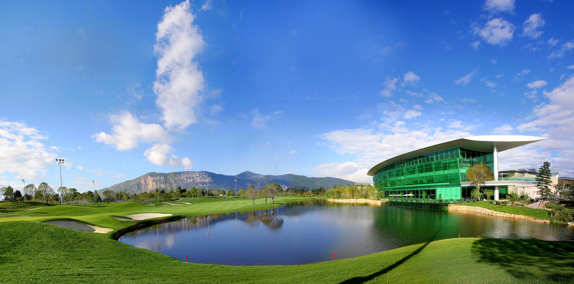 A modern golf clubhouse with glass walls overlooking a serene water feature.
