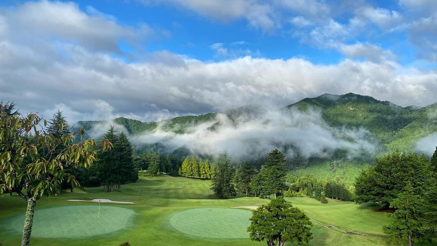 A serene golf hole set amidst misty mountains and dense greenery.