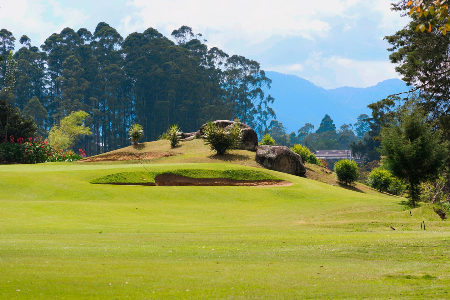 A golf hole nestled among rocks and trees with mountains in the background