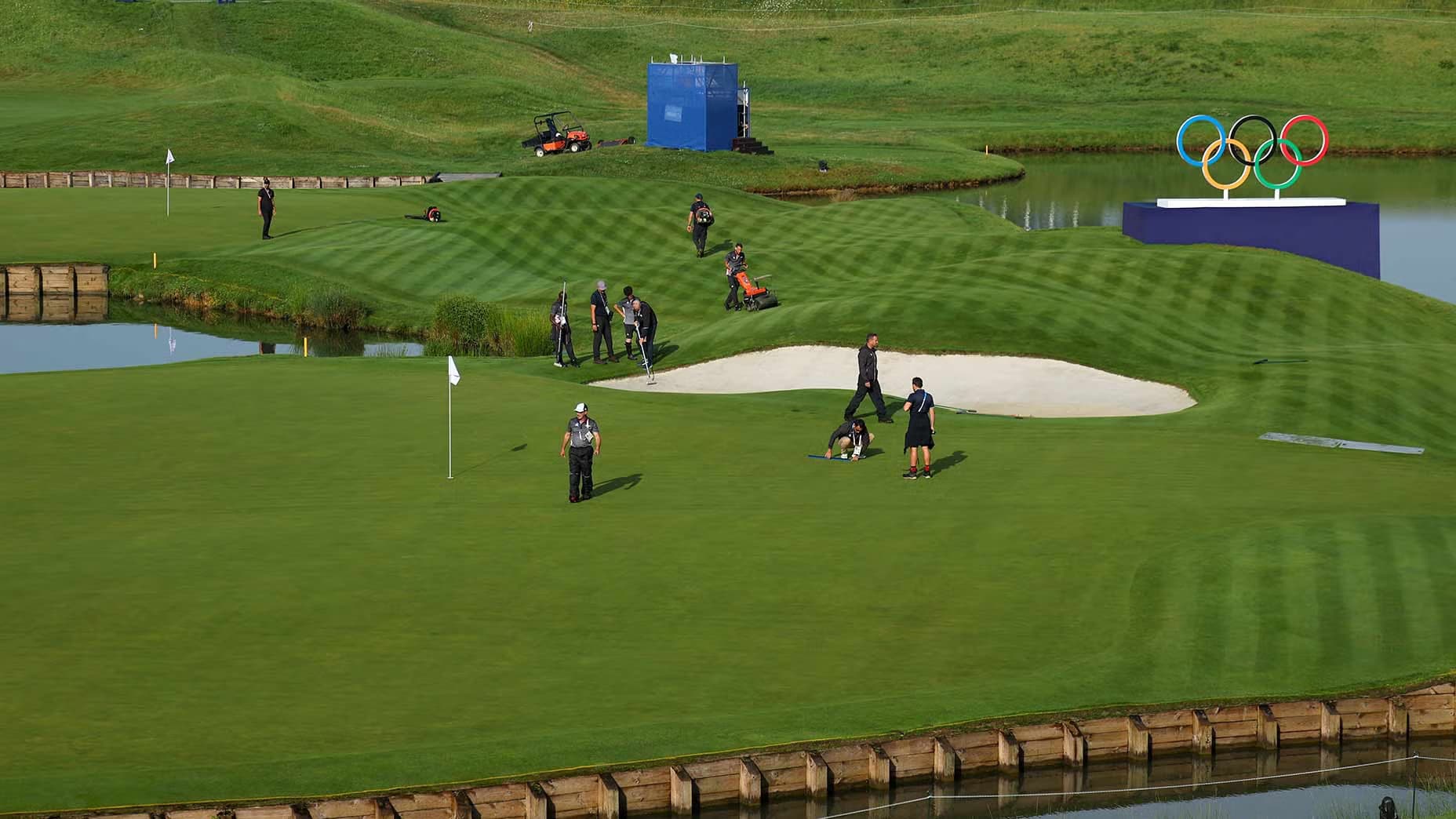 Undulating fairway with grounds staff preparing the course. Olympic logo is visible