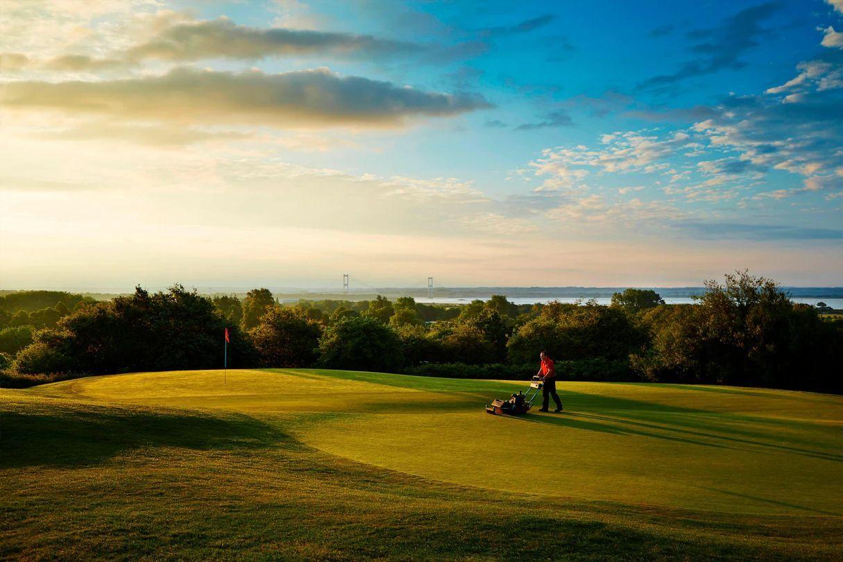 A golfer plays on a lush course at sunset with the view of a bridge in the background.