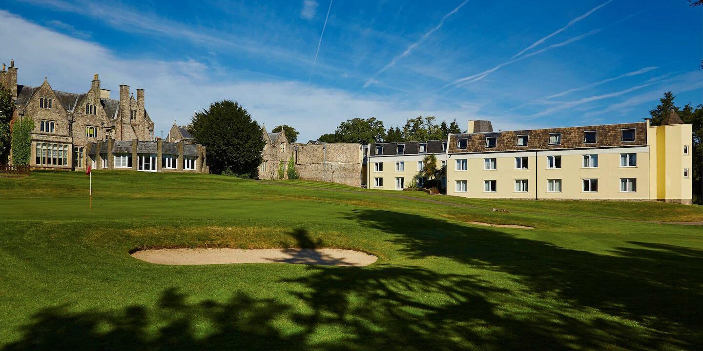 A golf green lies beside the historic manor house and modern hotel wing.