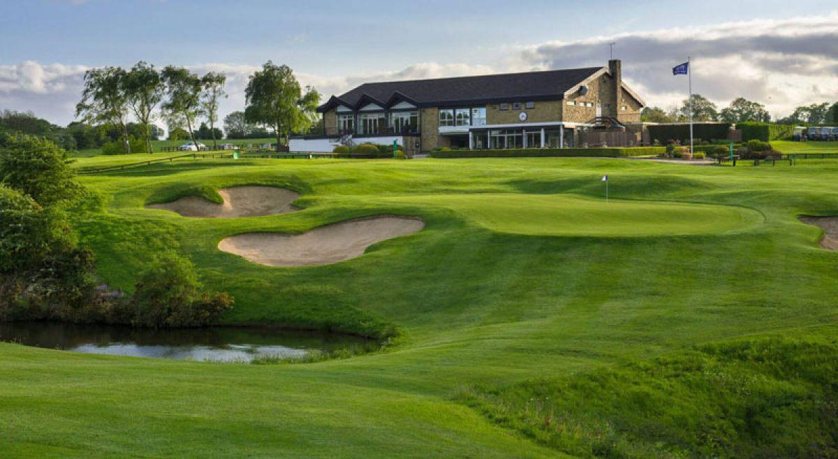 A golf clubhouse overlooking a green with multiple sand bunkers and a pond.