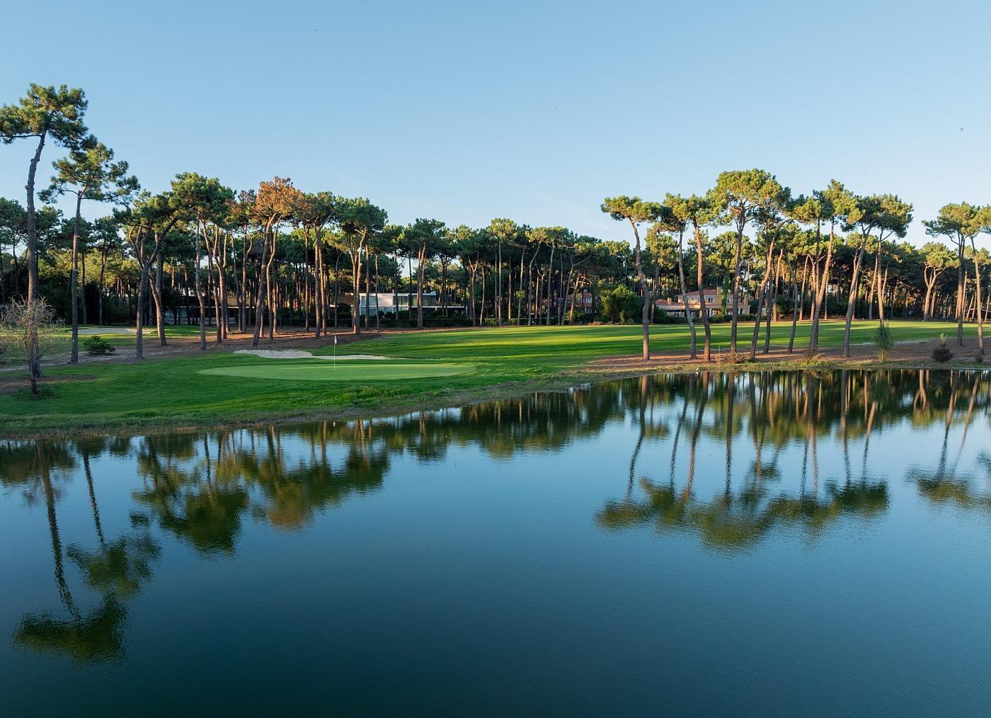 Tree-lined fairway leading to a green with water behind it