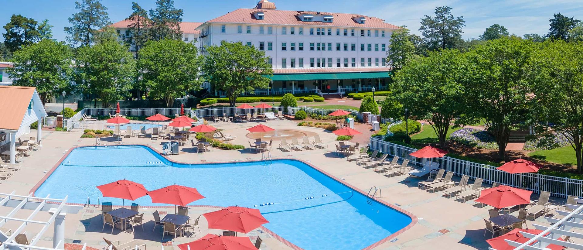 Panoramic view of Pinehurst’s outdoor pool featuring sun beds and red umbrellas