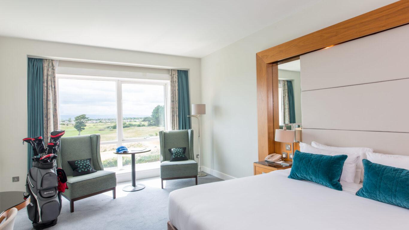 A hotel room with a golf course view and a golf bag by the window.