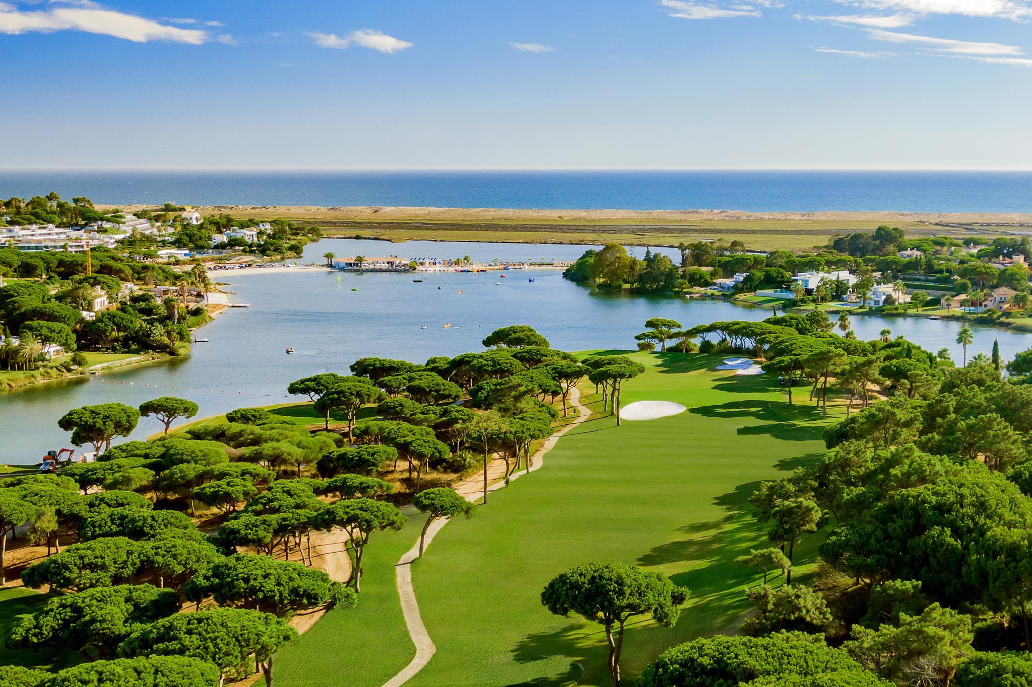Aerial view of a tree-lined fairway wit hwater at the back