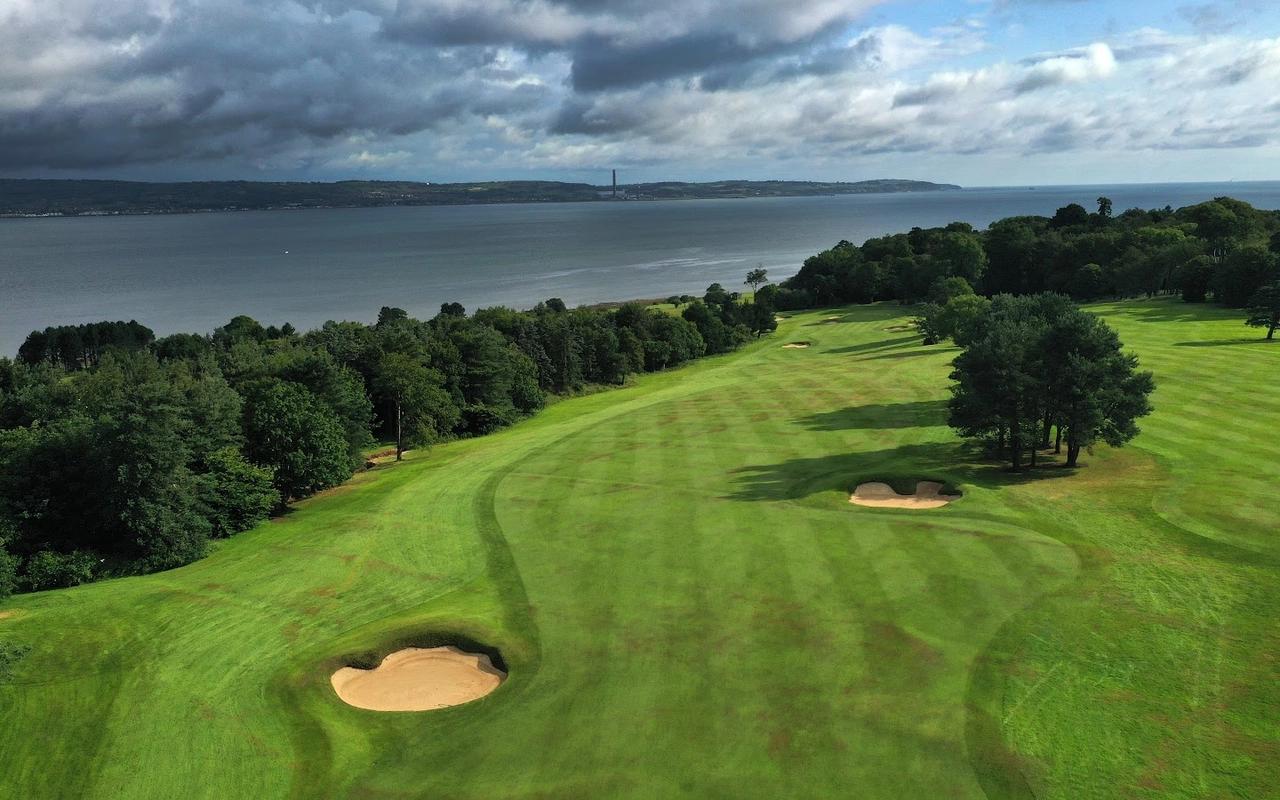 A sweeping fairway running alongside the lough, bordered by woodland and dramatic skies above.