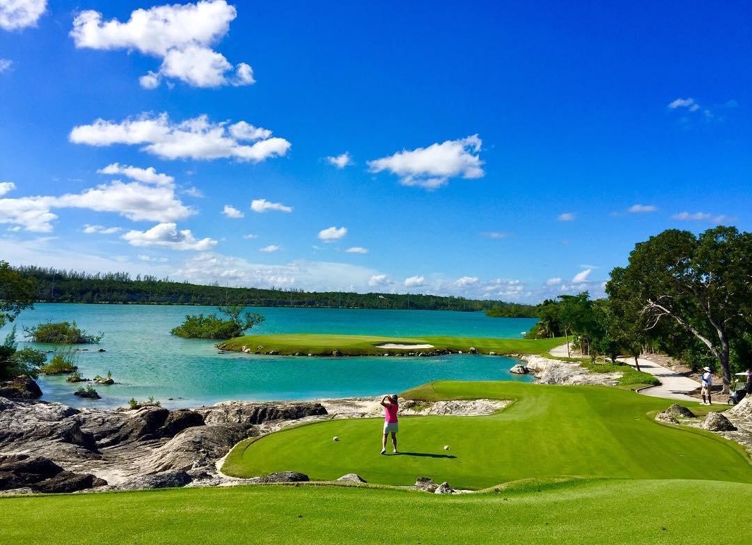 A golfer tees off toward a bright blue water hazard and island green.