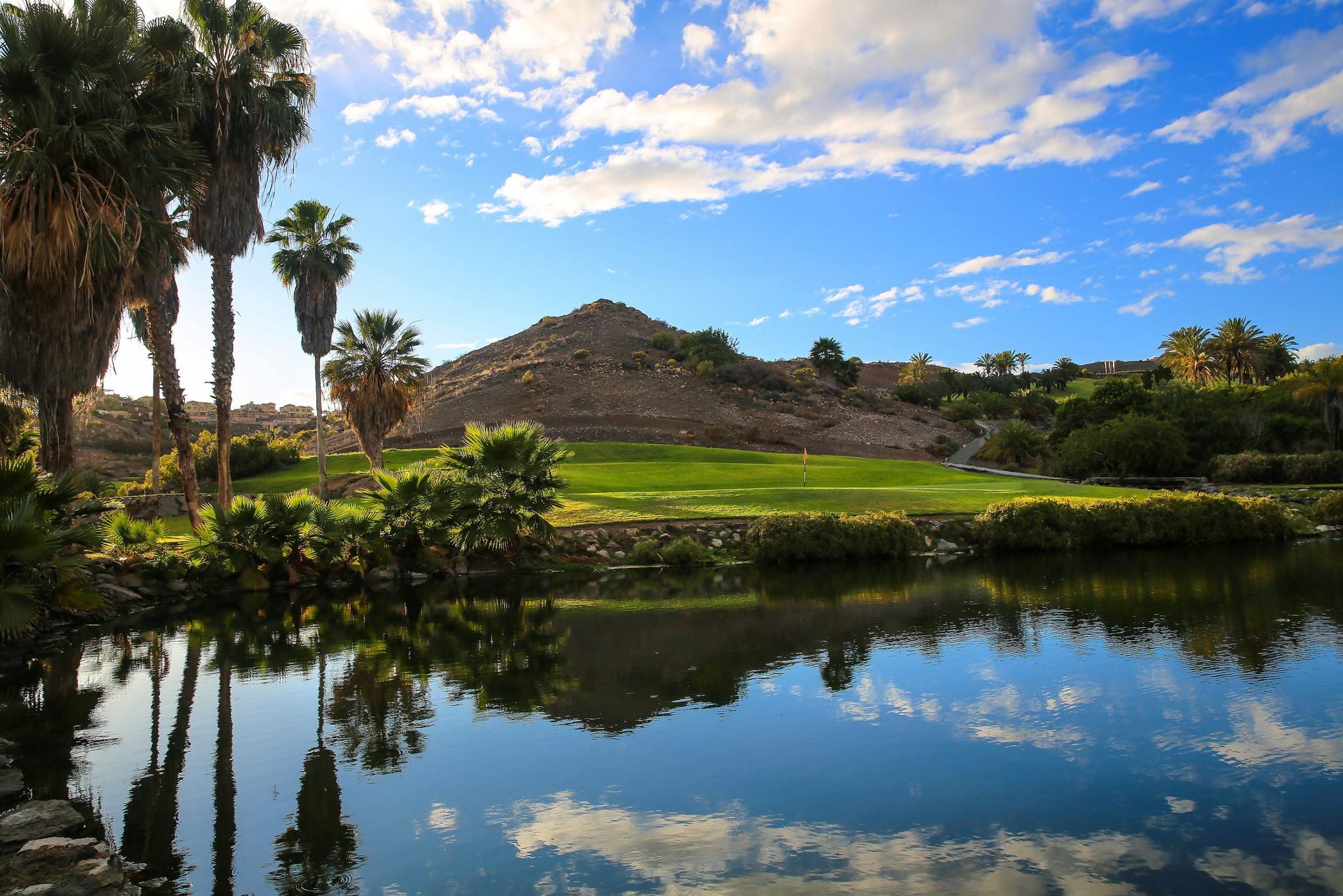 Water hazard in front of a green with hills behind it