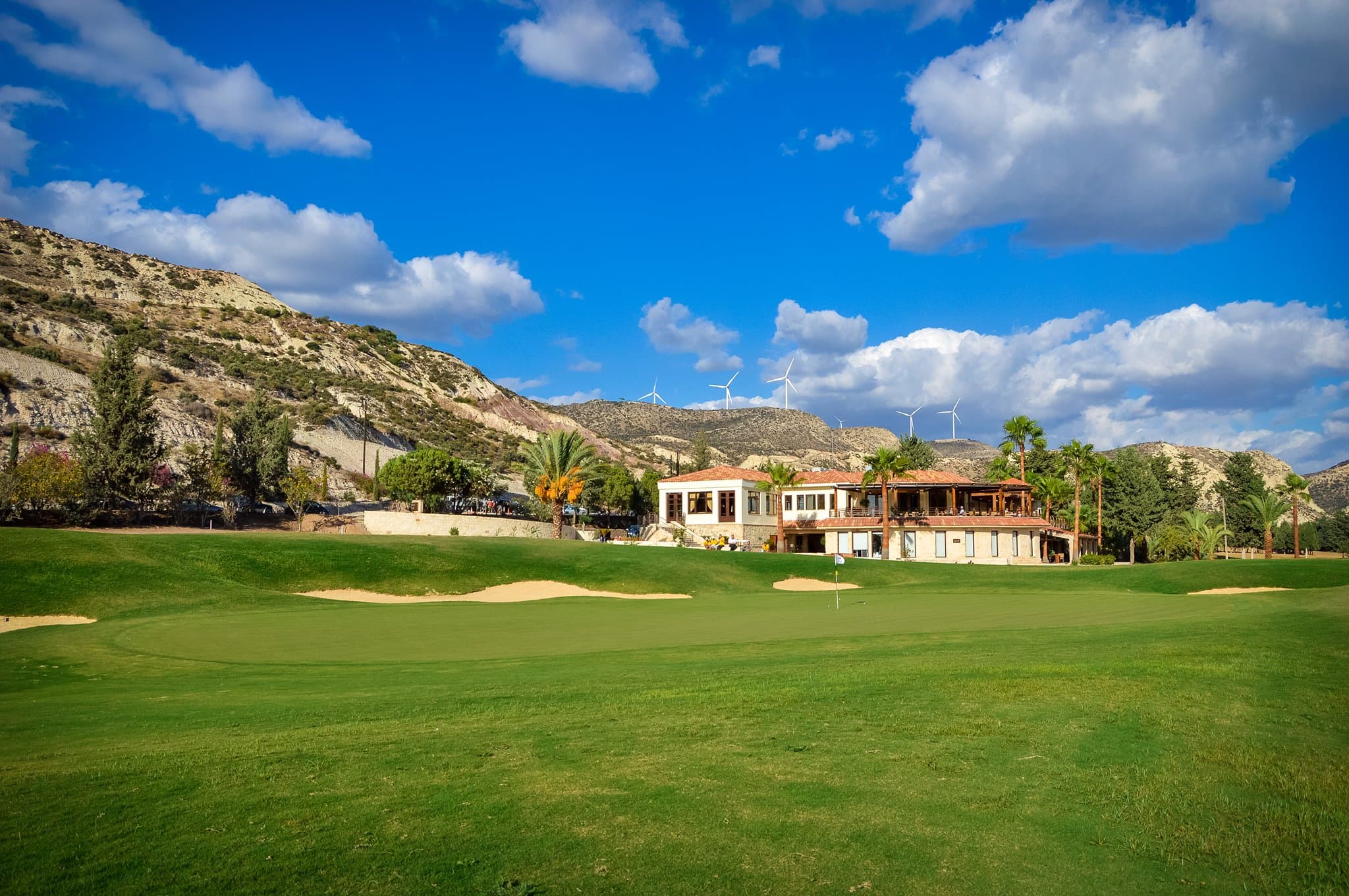 A clubhouse surrounded by palm trees and rolling hills.