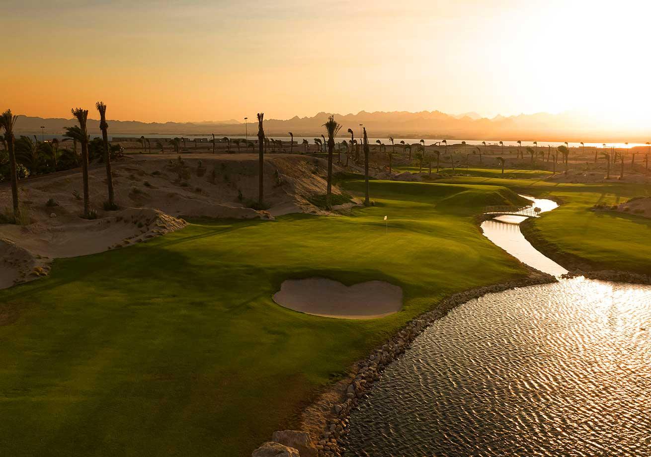 A smooth green placed next to a sand bunker and water hazard at sunset