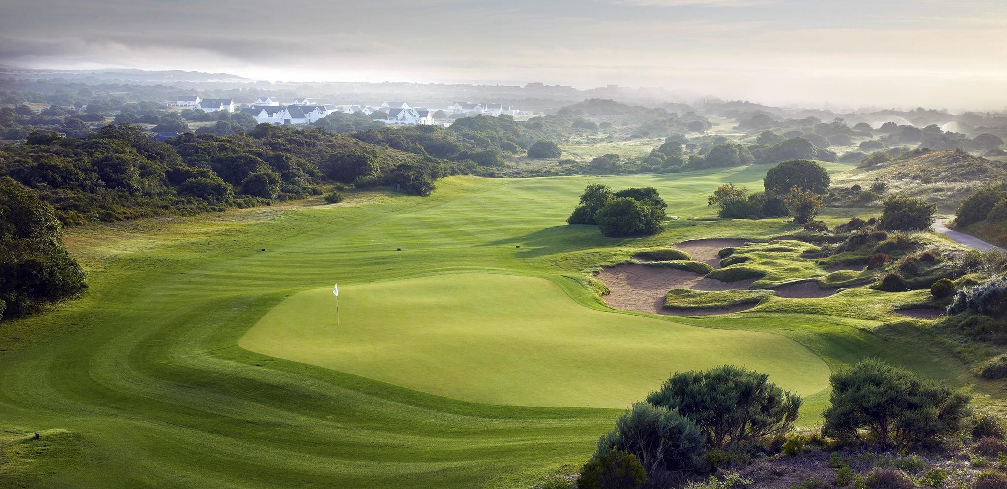 A misty morning view of a golf course with greens and bunkers set among natural vegetation.
