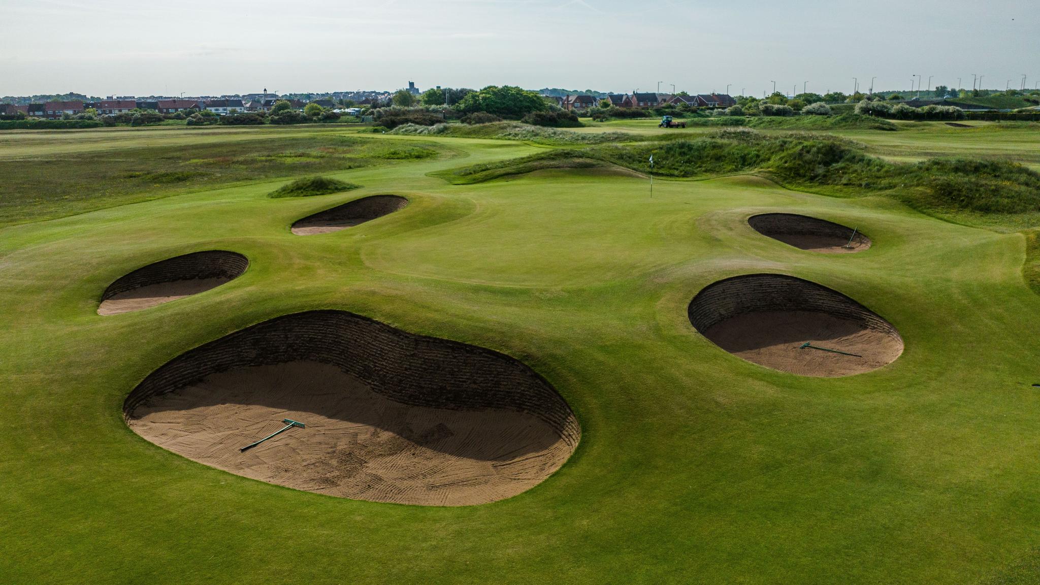 Deep, circular sand bunkers surround a green on a challenging golf hole.