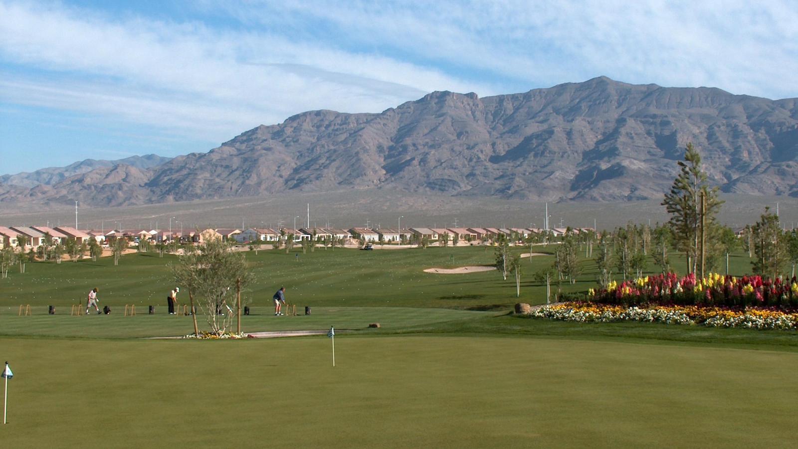 Golfers practicing their swing at the course with local town houses and mountains in the distance