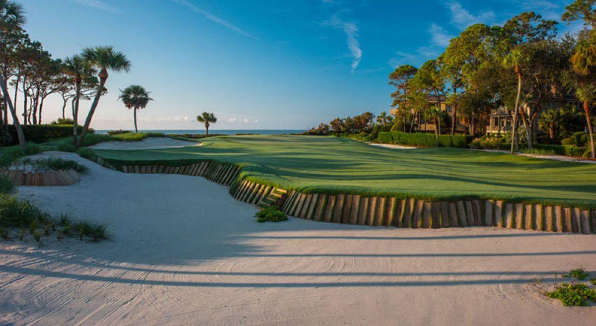 Fairway leading to a green with sea views elevated from a large sand bunker with a mood wall