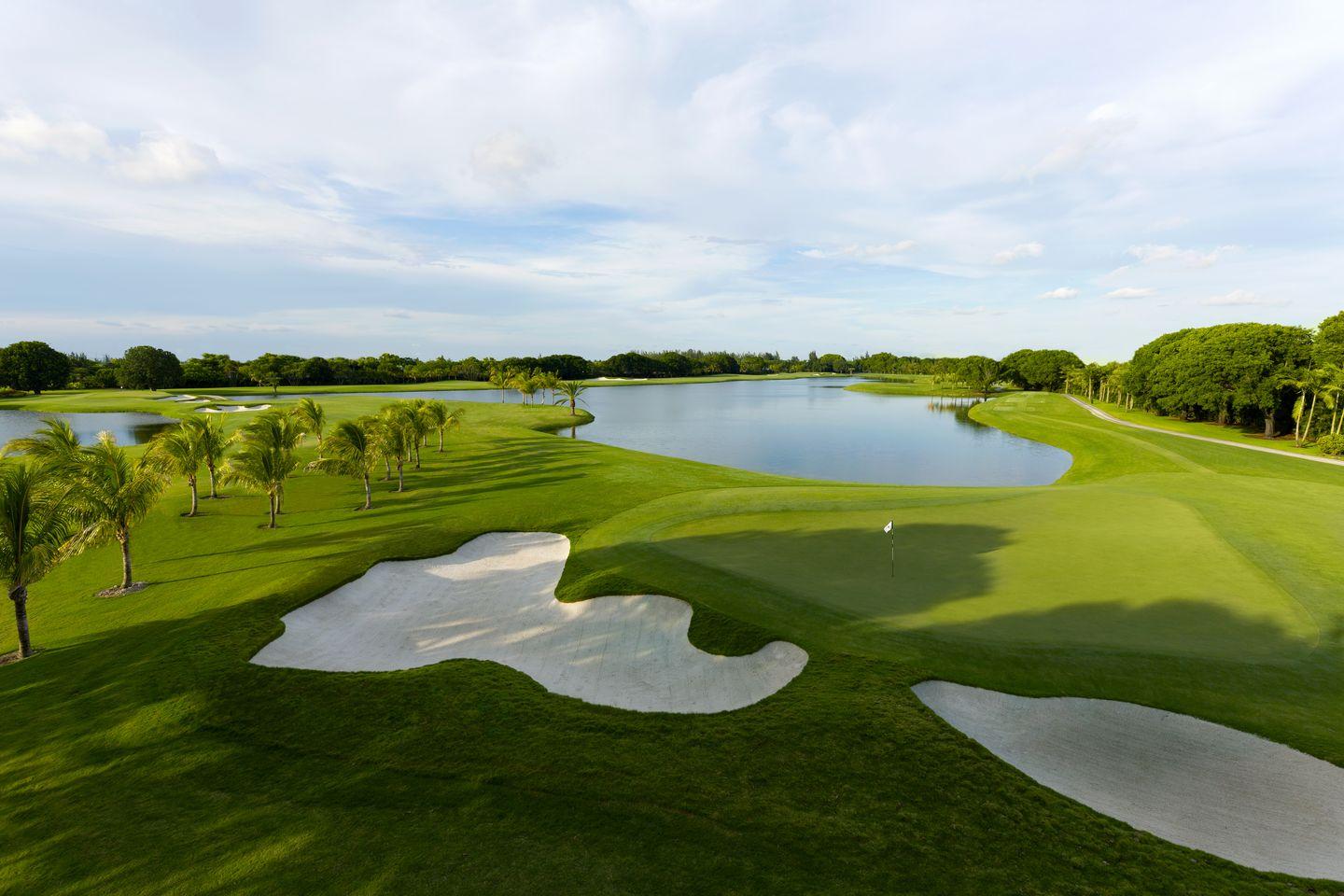 A stunning golf course with pristine fairways, surrounded by water hazards and palm trees under a bright sky.